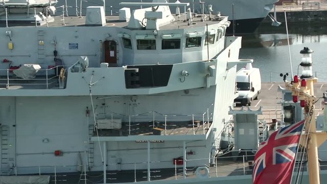Close tracking shot past Royal Navy Destroyer in Portsmouth Harbour with a red ensign in the foreground
