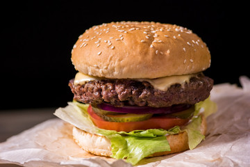 Burger on black background. Grilled meat and fresh vegetables.