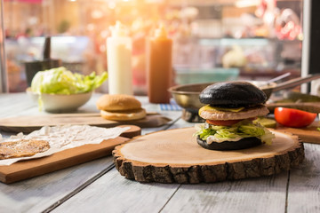 Black burger on wooden board. Cooking table with food.