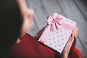 Gift with pink ribbon in female hands. Top view.