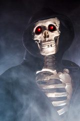 ein Skelett mit glühenden Augen und schwarzer Kapuze ist von Rauch umgeben und symbolisiert den Tod