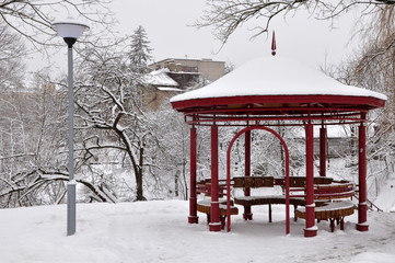 City park with trees and metal gazebo in snow in winter. Grodno, Belarus.