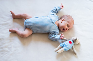 Cute newborn baby boy with teddy bear lying on bed