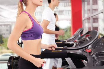 Fototapeta na wymiar Young sporty woman running on treadmill in gym, close up view