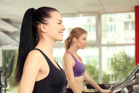 Young sporty woman running on treadmill in gym