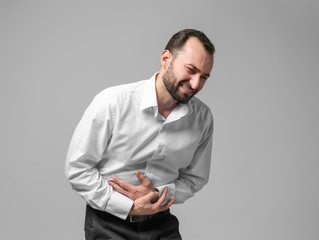 Handsome man suffering from abdominal pain, on color background