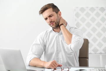 Handsome man suffering from neck pain in office