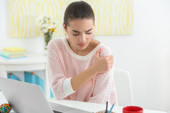 Beautiful young woman suffering from shoulder pain in office