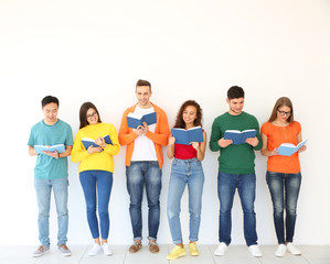 Group of people reading books while standing near light wall