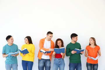 Group of people reading books while standing near light wall