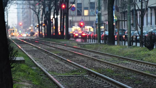Tram di Milano viaggia di notte su linea a doppio binario e sullo sfondo passaggio pedonale e traffico cittadino con luci della citt&agrave; e semafori
