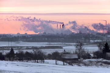 Working Nitrogen Plant in smoke on the background of dawn in winter. Abandoned village in the foreground. Grodno, Belarus.