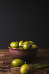 Green olives, bay leaf on a wooden board.  Olives on a black  background. Copyspace