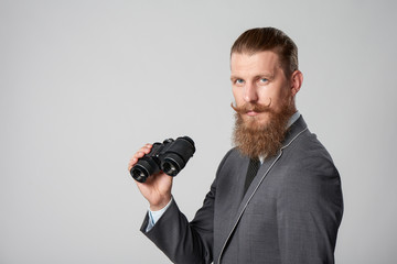 Closeup portrait of bearded hipster business man in suit holding binoculars