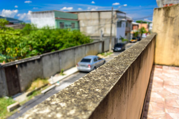 Fototapeta na wymiar The moldy wall and blurry street with cars and houses in Bangu neighborhood, where the prison, the Penitentiary Complex of Gericino and Bangu dump are located, the West Zone of Rio de Janeiro, Brazil