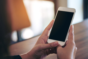 Mockup image of hands holding white mobile phone with blank white screen on vintage wood table in the room