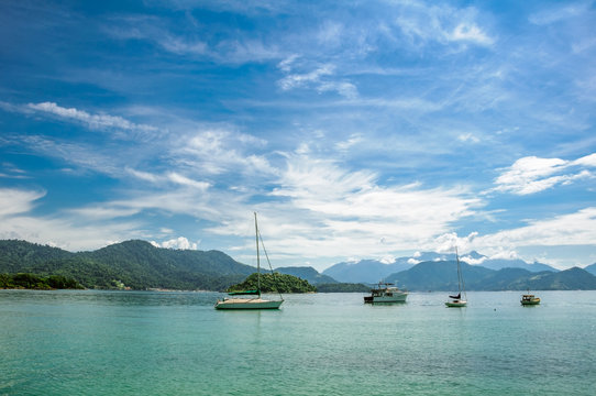 Boats floating in the turquoise water against the background of mountains and beautiful blue sky with spindrift clouds next to Ilha Grande, Angra dos Reis, RJ, Brazil