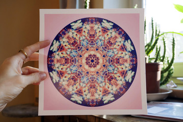 Hand holding abstract mandala picture inside home interior
