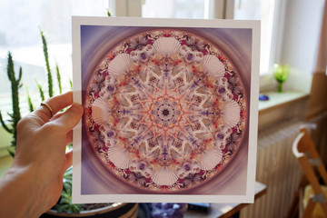 Hand holding abstract mandala picture inside home interior