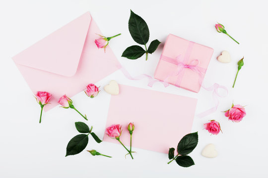 Gift or present box, envelope, paper blank and pink rose flower on white table from above in flat lay style for greeting card on Womans day.