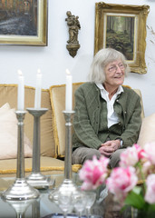 Seniorin sitzt alleine in ihrem Wohnzimmer und lächelt