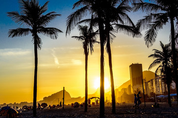 Obraz premium Beautiful bright sunset on Copacabana beach with palm trees and silhouettes of people walking at the beach, Rio de Janeiro, Brazil