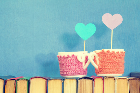 Valentines day concept. Two cups with blue paper heart and violet paper heart  on books over blue background.