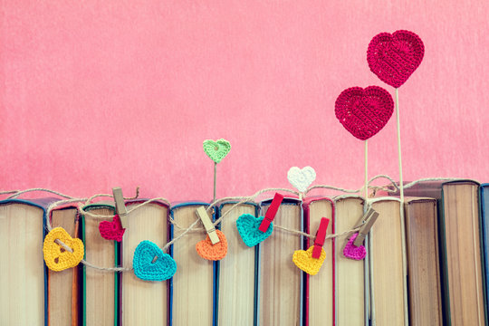 Valentines day concept. Many multicolor crochet hearts on books over pink background.