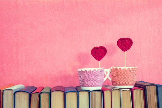 Valentines day concept. Two cups with red crochet hearts on books over pink background.