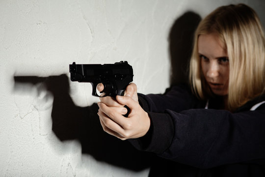 serious girl with gun aiming on wall background with copyspace