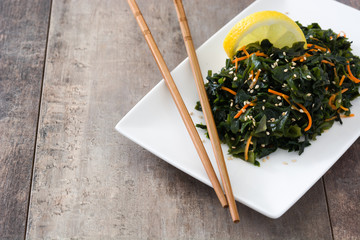 Wakame salad with carrot, sesame seeds and lemon juice in plate on wooden table
