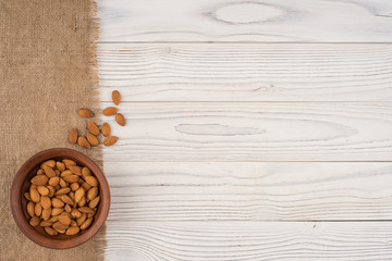 Almonds in a brown bowl and old white wooden table.