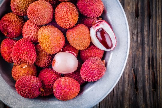 Fresh organic lychee fruit in a bowl on wooden background. Top view