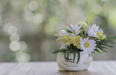 Artificial flowers in a vase on wood and background bokeh.