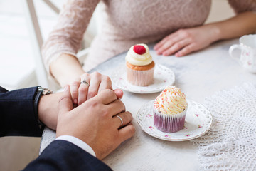 Two young people holding hands, breakfast, tea with cupcake, selective focus