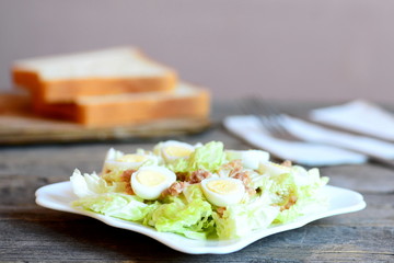 Chinese cabbage salad with canned tuna and quail eggs dressing with olive oil and lemon juice. Cabbage salad on plate, bread slices on wooden table. Simple and quick salad recipe. Closeup