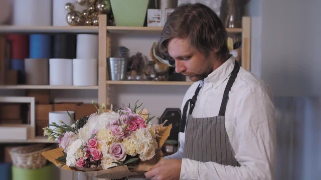 happy smiling florist man making fashion bunch at flower shop. people, business, sale and floristry concept. Bouquet with roses, peone, lilac and lisianthus