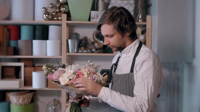 happy smiling florist man making fashion bunch at flower shop. people, business, sale and floristry concept. Bouquet with roses, peone, lilac and lisianthus