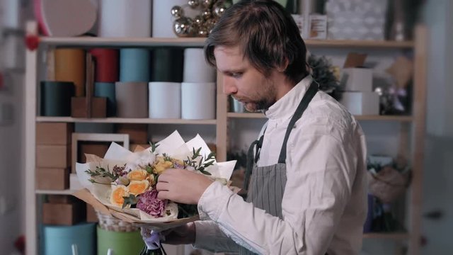 happy smiling florist man making bunch at flower shop. people, business, sale and floristry concept. Bouquet with roses, peone, lilac and lisianthus