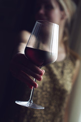 woman with gold spangle dress offering a glass of red wine