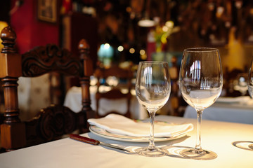 Fototapeta na wymiar Empty glasses in a restaurant on white tablecloth. Shade, brown background and carved chairs.