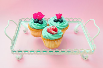 Cupcakes with butter cream and vanilla with raspberry and blueberry with pink flowers on the tray on pink background