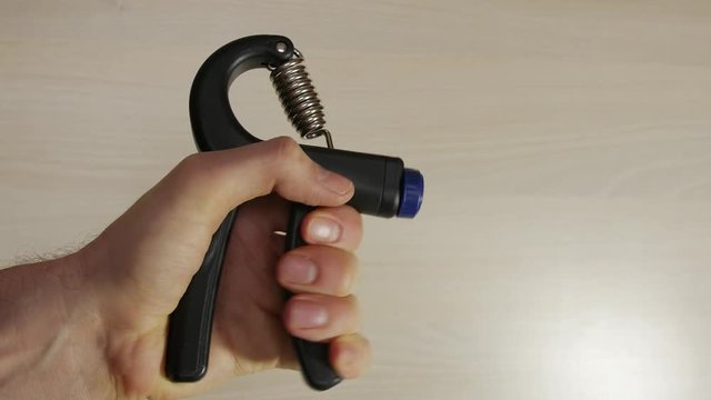 Man squeezes hand grip, strengthens muscles in hand, fingers, wrist, arm, as part of routine exercise workout, light background.