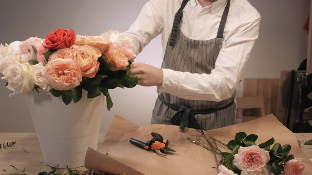 Male florist hands closeup, cuts rose for bouquet in flower shop. Man assistant or owner in floral design studio, making decorations and arrangements. Flowers delivery, creating order. Small business.