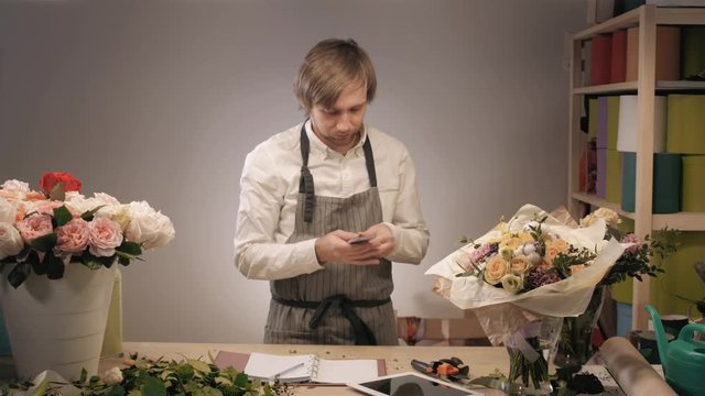 Photo of smiling florist standing with a colorful bouquet in flower shop. Bouquet with roses, peone, lilac and lisianthus