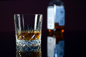 Glass of whiskey on black table with beautiful reflection.