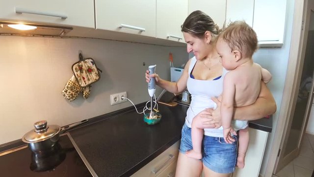 Young beautiful mother holding her baby son and cooking on kitchen