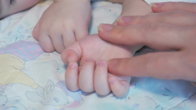 Handheld shot - mother caressing sleeping baby's hand. Closeup