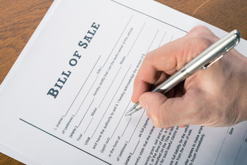 man's hand with a pen sign the bill of sale