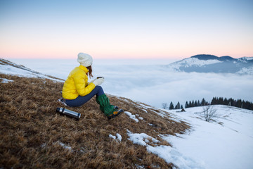 Young woman hiking in winter mountains. Woman drinking warm tea in the mountai.